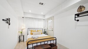 A neatly arranged bedroom with a bed, bedside table, lamp, and a small wooden chest. - PRIVATE 2BR GUESTHOUSE: Food Hub & Easy Freeway Access in International District (Houston)