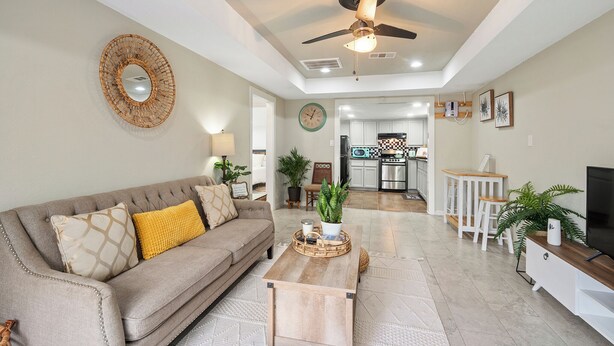 A living room with a sofa, coffee table, and a ceiling fan. There is a kitchen in the background with a microwave and a refrigerator. - PRIVATE 2BR GUESTHOUSE: Food Hub & Easy Freeway Access in International District (Houston)
