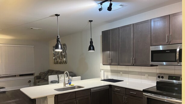 Une cuisine moderne avec des meubles de couleur sombre, des appareils en acier inoxydable et des luminaires suspendus.