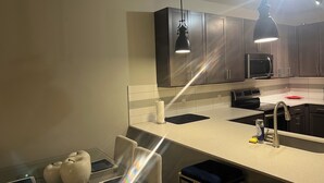 Une cuisine moderne avec des meubles de couleur sombre, un plan de travail blanc, un évier en acier inoxydable et un micro-ondes noir.