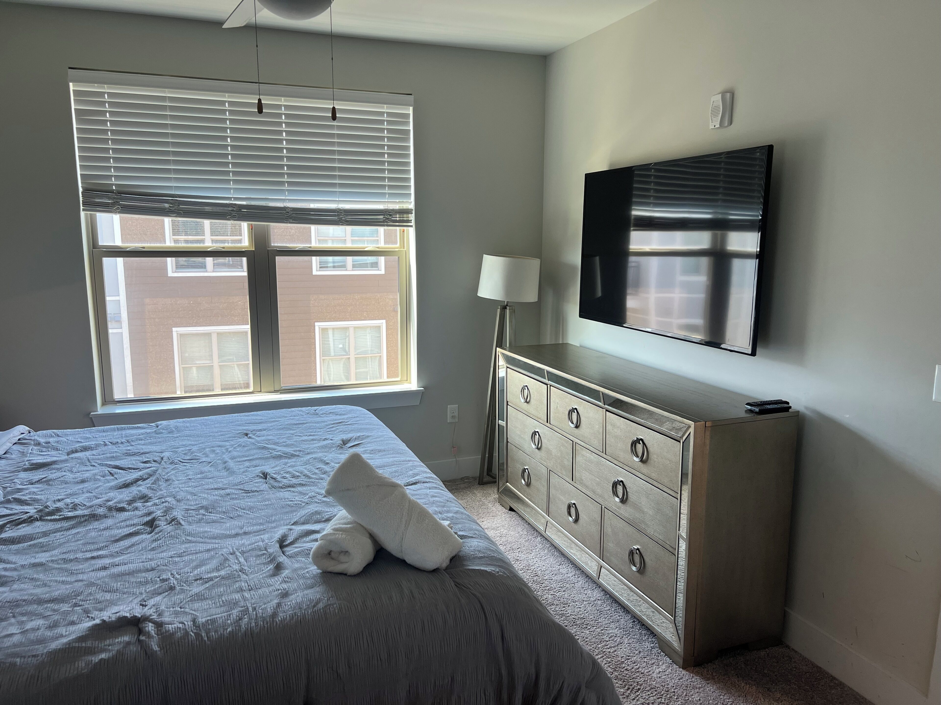 A bedroom with a bed, a dresser, a TV, and a window with blinds.
