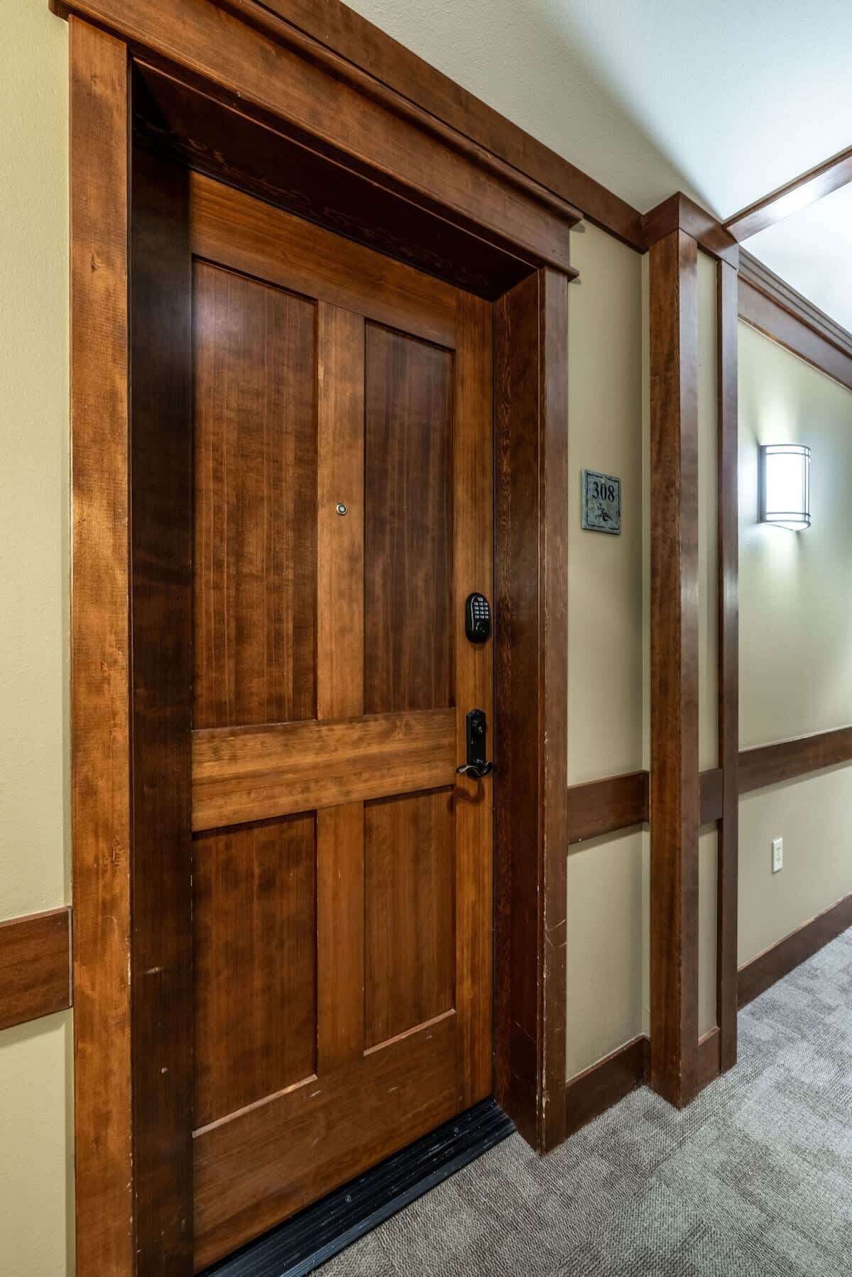 Una puerta de madera con cerradura electrónica, una placa con números y un accesorio de iluminación en la pared.