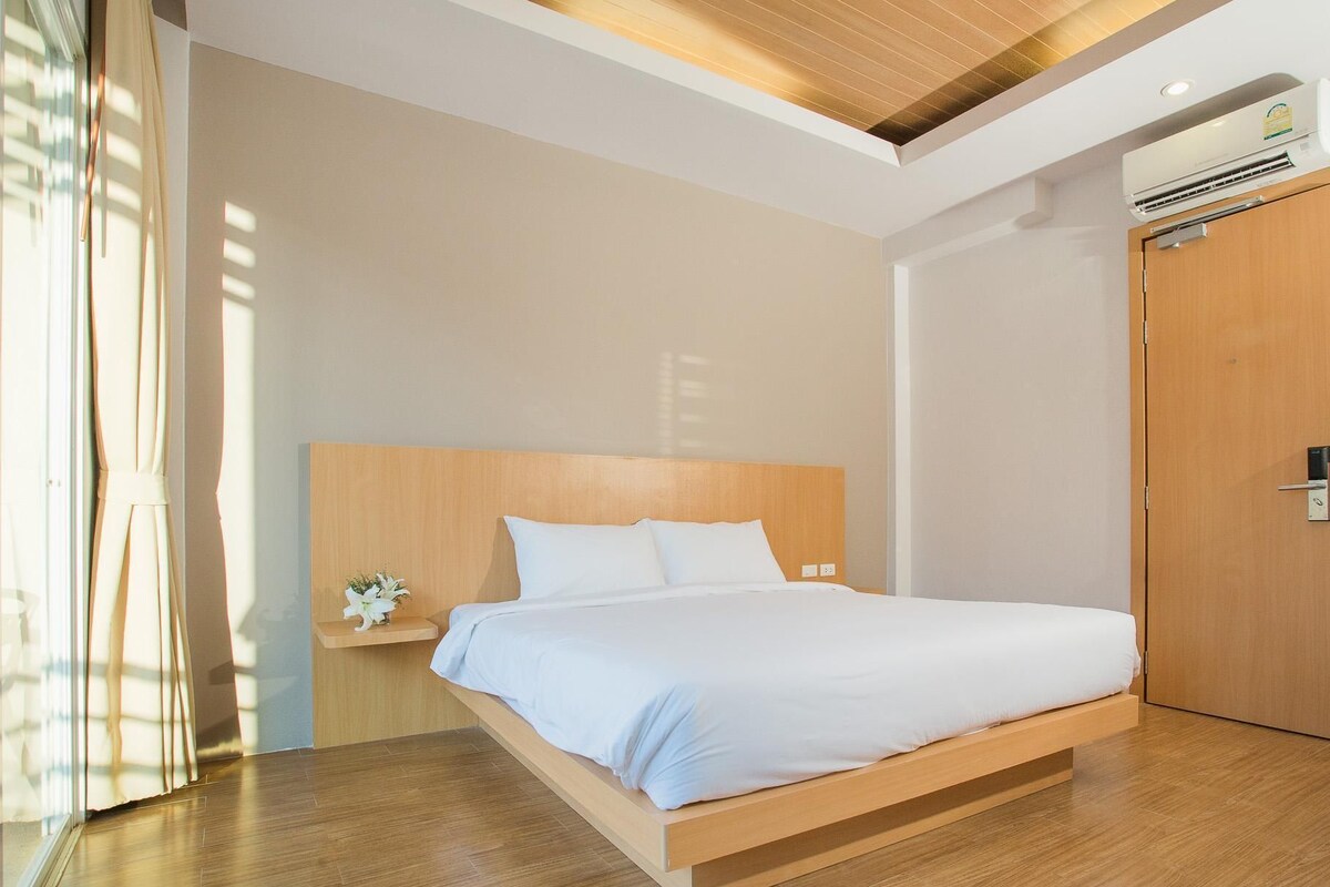 Camera d'albergo moderna con un letto a baldacchino in legno, un comodino con un vaso di fiori e un'ampia finestra con tende.