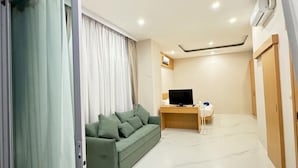 Un soggiorno moderno con un divano verde, una TV su un mobile in legno e una porta vetrata scorrevole che dà su un balcone.