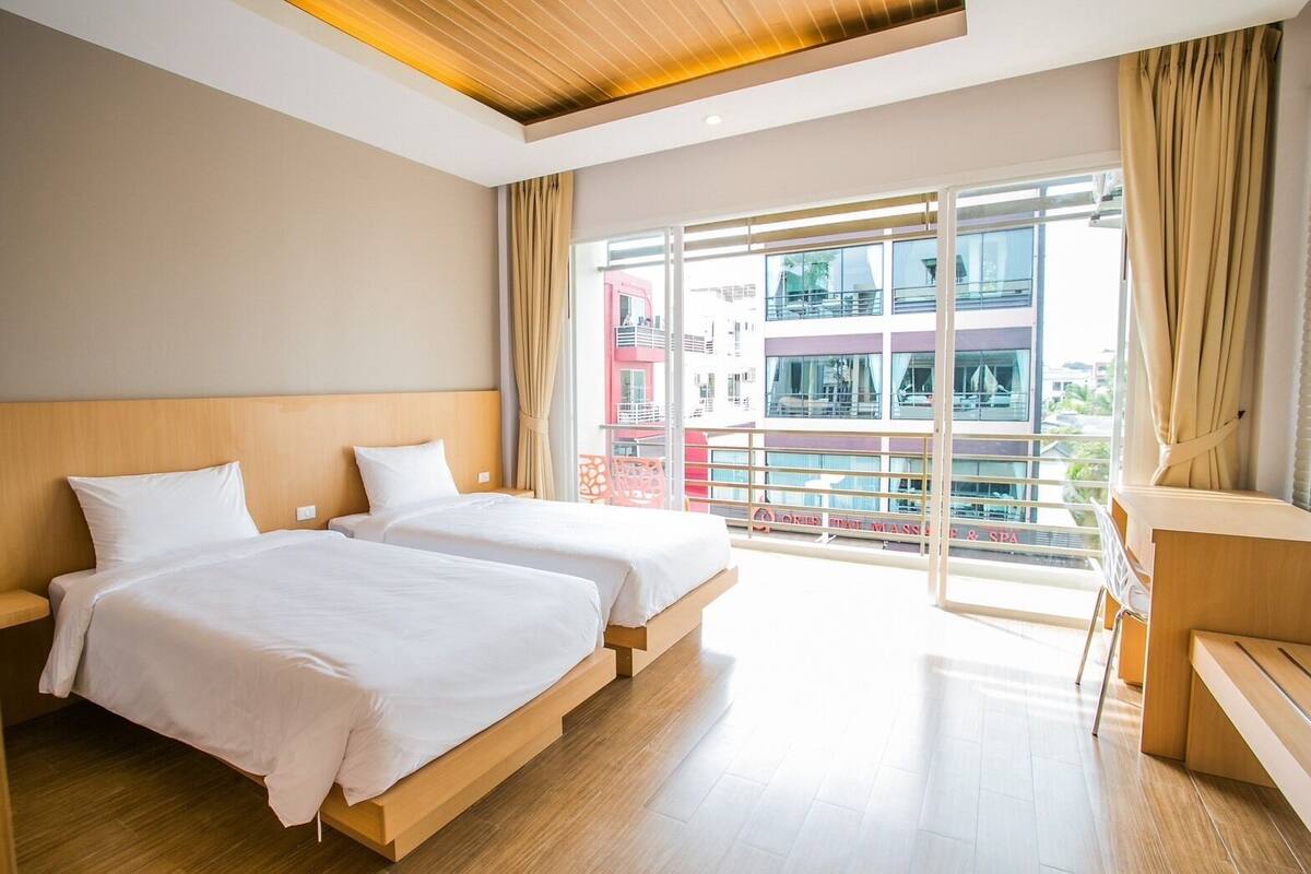A hotel room with two beds, a wooden headboard, a large window with a view of a building and a balcony.