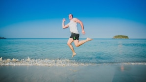Una persona salta su una spiaggia con acqua cristallina e un'isola in lontananza.