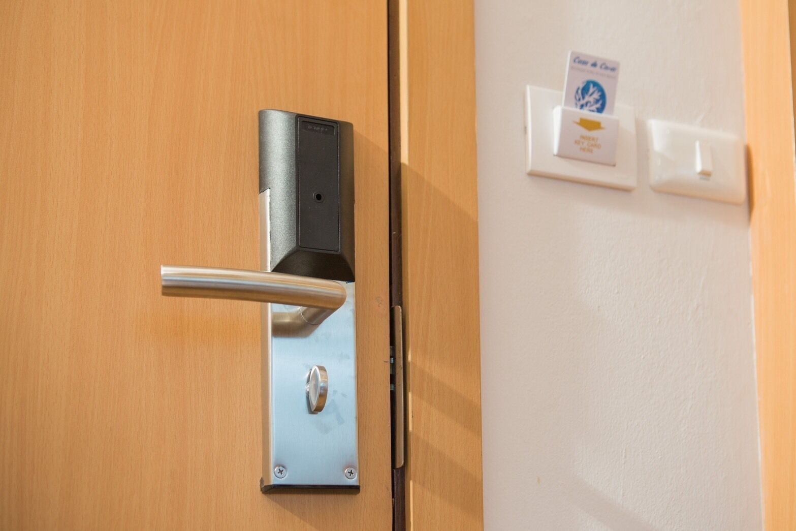 A modern door with a metallic handle and a keyhole, a card reader, and a light switch on the wall.