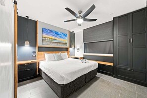 Une chambre à coucher moderne avec un lit, un ventilateur de plafond, un téléviseur et un tableau au mur.
