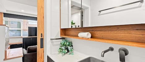 A modern bathroom with a large mirror, a wooden shelf, a sink, and a towel rack.