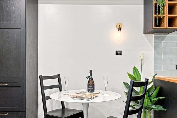 A dining area with a round table, two chairs, a bottle of sparkling wine, and two glasses.