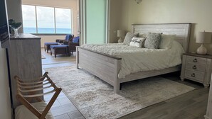 A bedroom with a bed, bedside tables, a chair, a desk, and a view of the ocean. - Oceanfront 3BR Condo, Pool, Direct Beach Access (Cole Bay)