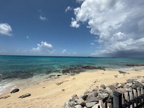 A beach with clear turquoise water, a sandy shore, and a rocky breakwater. - Oceanfront 3BR Condo, Pool, Direct Beach Access (Cole Bay)