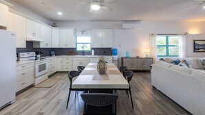 A modern kitchen with white cabinets, a dining table with chairs, a ceiling fan, and a window with curtains. - Oceanfront 3BR Condo, Pool, Direct Beach Access (Cole Bay)