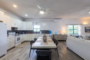 A modern kitchen with white cabinets, a dining table with chairs, a ceiling fan, and a window with curtains. - Oceanfront 3BR Condo, Pool, Direct Beach Access (Cole Bay)