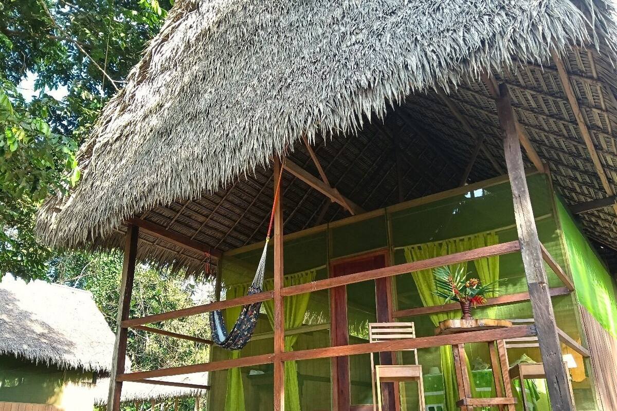 Een rieten hut met houten frame, een hangmat en een raam met gordijnen.