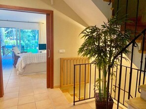 Una escalera con una planta en maceta, baranda de madera y vista a un dormitorio con cama y ventana.