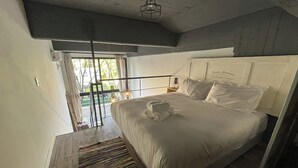 A bedroom with a large bed, a wooden floor, a view through a glass door, and a ceiling light fixture. - Rent Up - Luminoso Duplex en la Boca (Buenos Aires)
