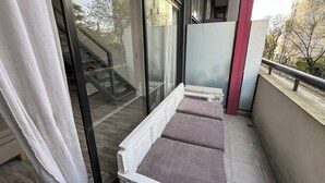 A balcony with a white railing, a glass door, and a view of a building and trees. - Rent Up - Luminoso Duplex en la Boca (Buenos Aires)