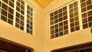 A spacious living room with high ceilings, large windows, a wooden floor, and a cozy seating area with a sofa and armchairs. - Pax & Opis Luxury Villa (Mussoorie)