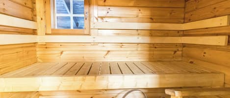 Ein Holzsaunaraum mit Bänken, einem Fenster und einem Eimer mit einem Holzlöffel.