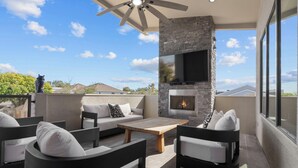 Eine moderne Außenpatio mit Kamin aus Stein, bequemen Sitzgelegenheiten und einem Deckenventilator.
