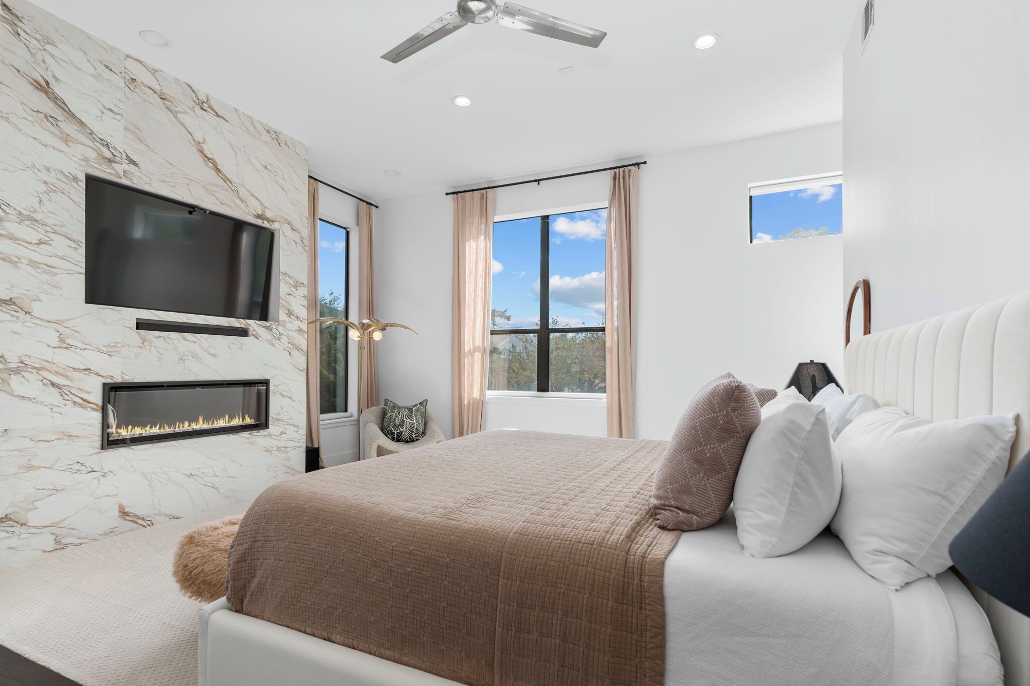 A modern bedroom with a marble wall, a fireplace, a bed with pillows, and a ceiling fan.