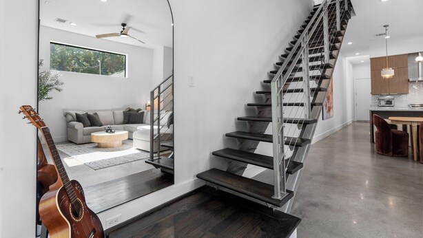Ein modernes Interieur mit Treppe, Wohnbereich inklusive Sofa und Couchtisch sowie Küchenzeile.