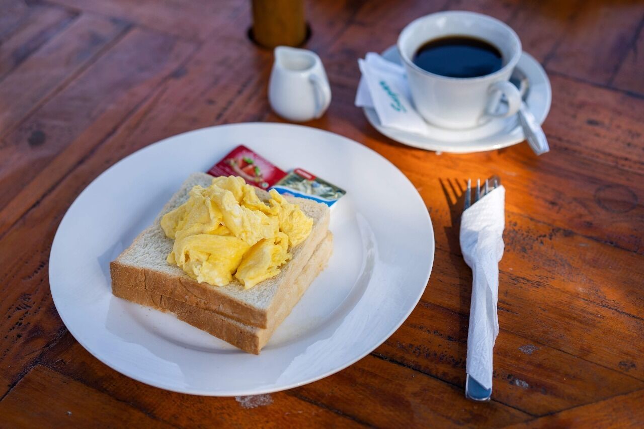 En tallrik med rörägg på rostat bröd, en kopp kaffe och en gaffel på ett träbord.