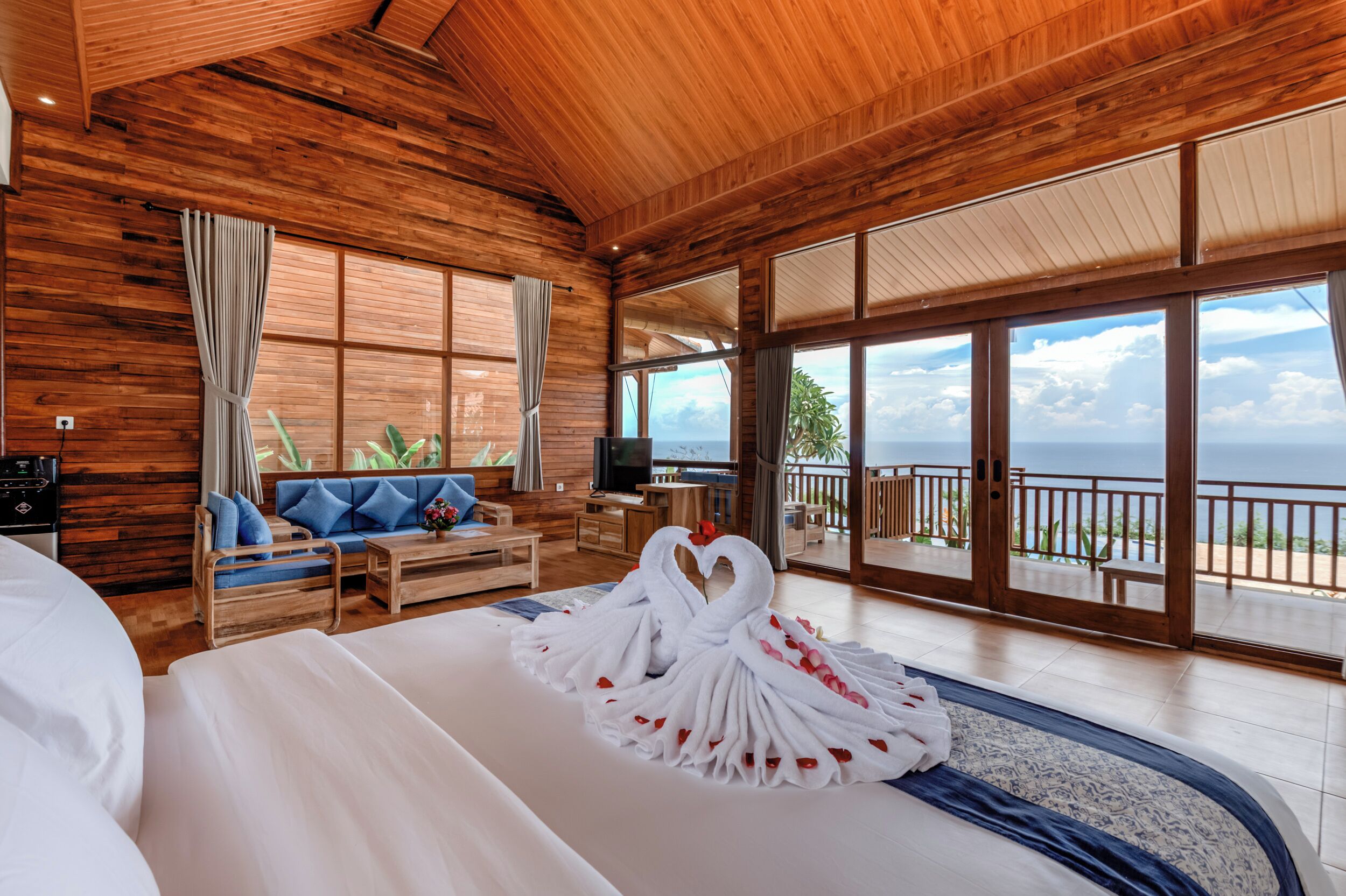 Een ruime kamer met een groot bed, houten wanden, een balkon met uitzicht en een decoratieve handdoek in de vorm van een zwaan.