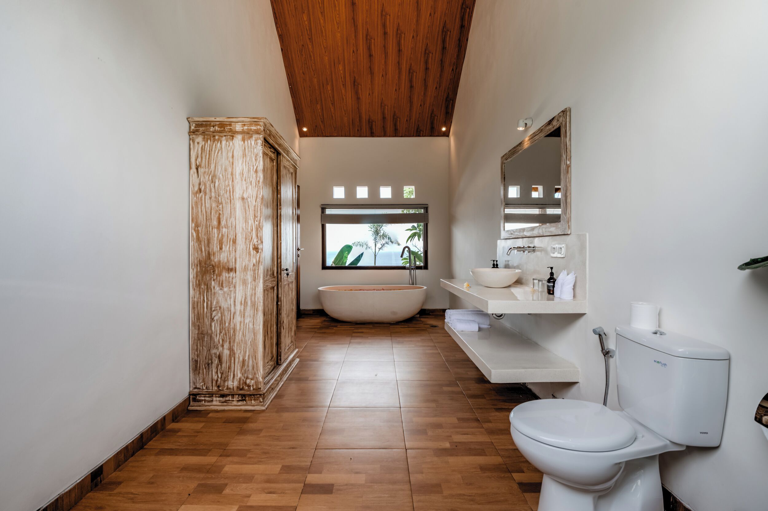 A modern bathroom with a wooden ceiling, a freestanding bathtub, a white sink, and a toilet.