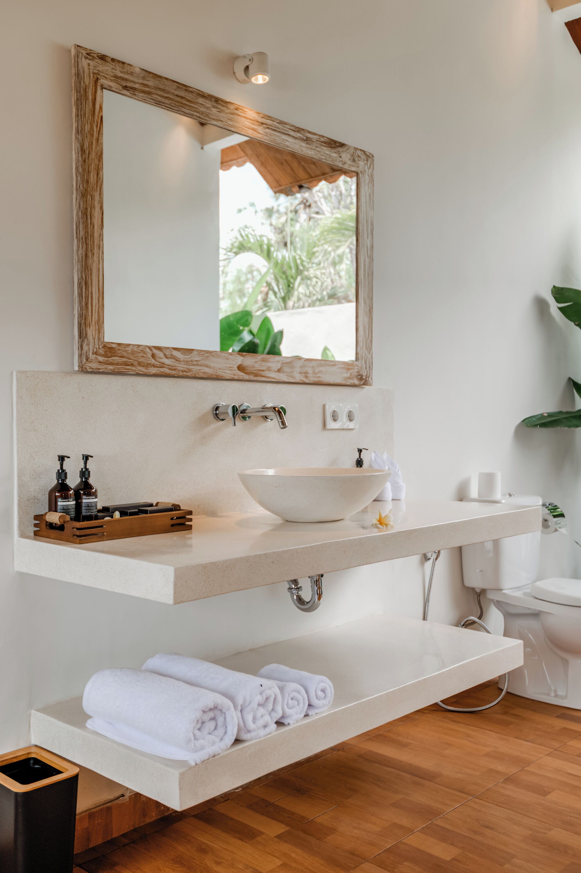 A bathroom with a white sink, a wooden-framed mirror, and a shelf with towels.