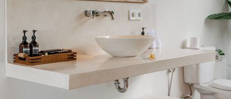 A bathroom with a white sink, a wooden-framed mirror, and a shelf with towels.