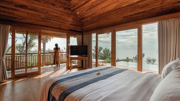 A bedroom with a large bed, wooden ceiling, and a balcony with a TV. - Seraya Cove Estate by Manara (Karangasem)