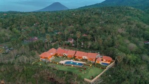 An aerial view of a resort with multiple buildings, a swimming pool, and a mountainous backdrop. - Seraya Cove Estate by Manara (Karangasem)