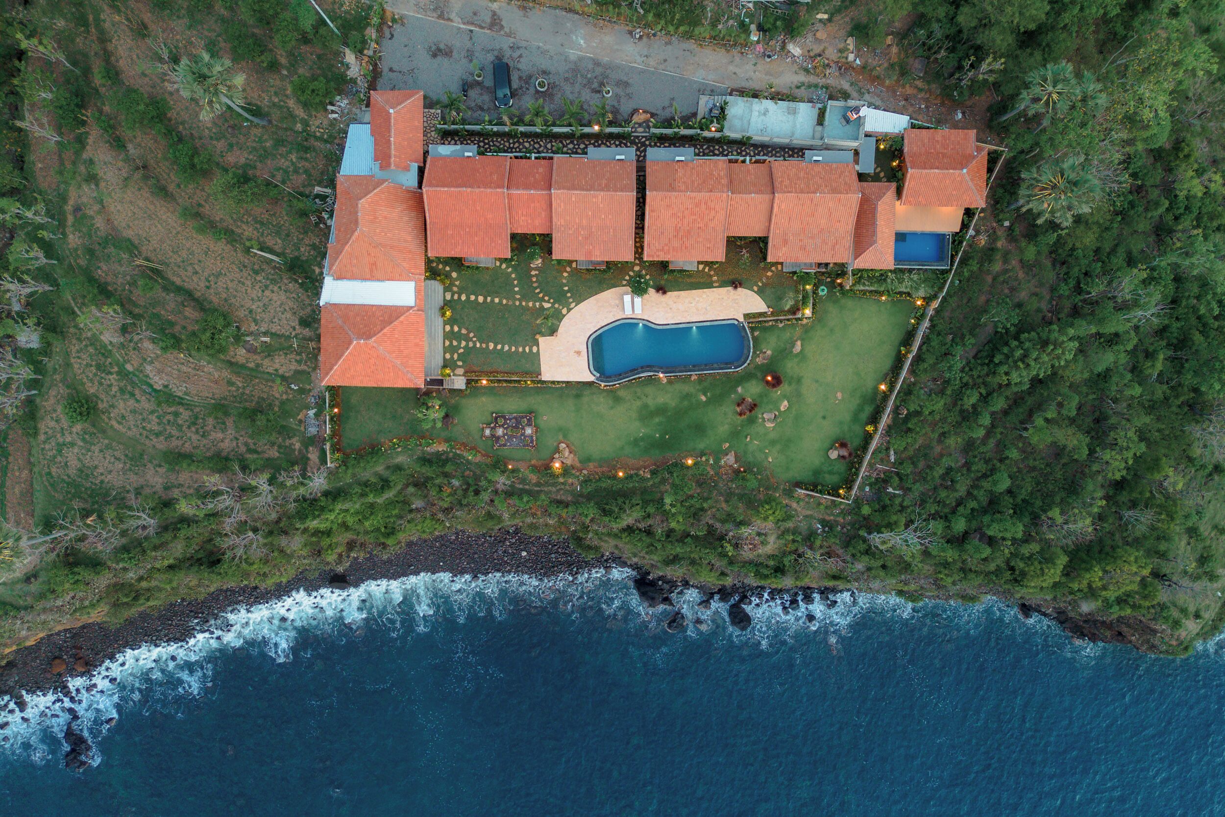 Vista aérea de una propiedad costera con piscina, varios edificios y una zona de playa.