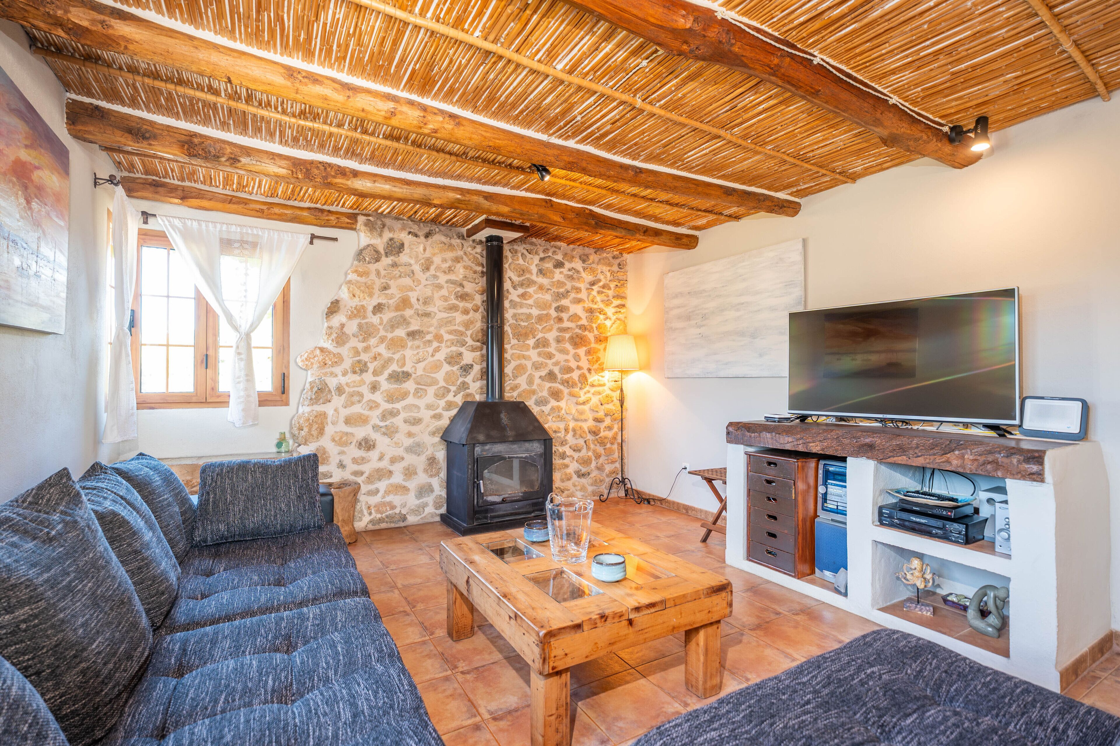 A cozy living room with a stone wall, a wooden ceiling, a sofa, a coffee table, a TV, and a fireplace.