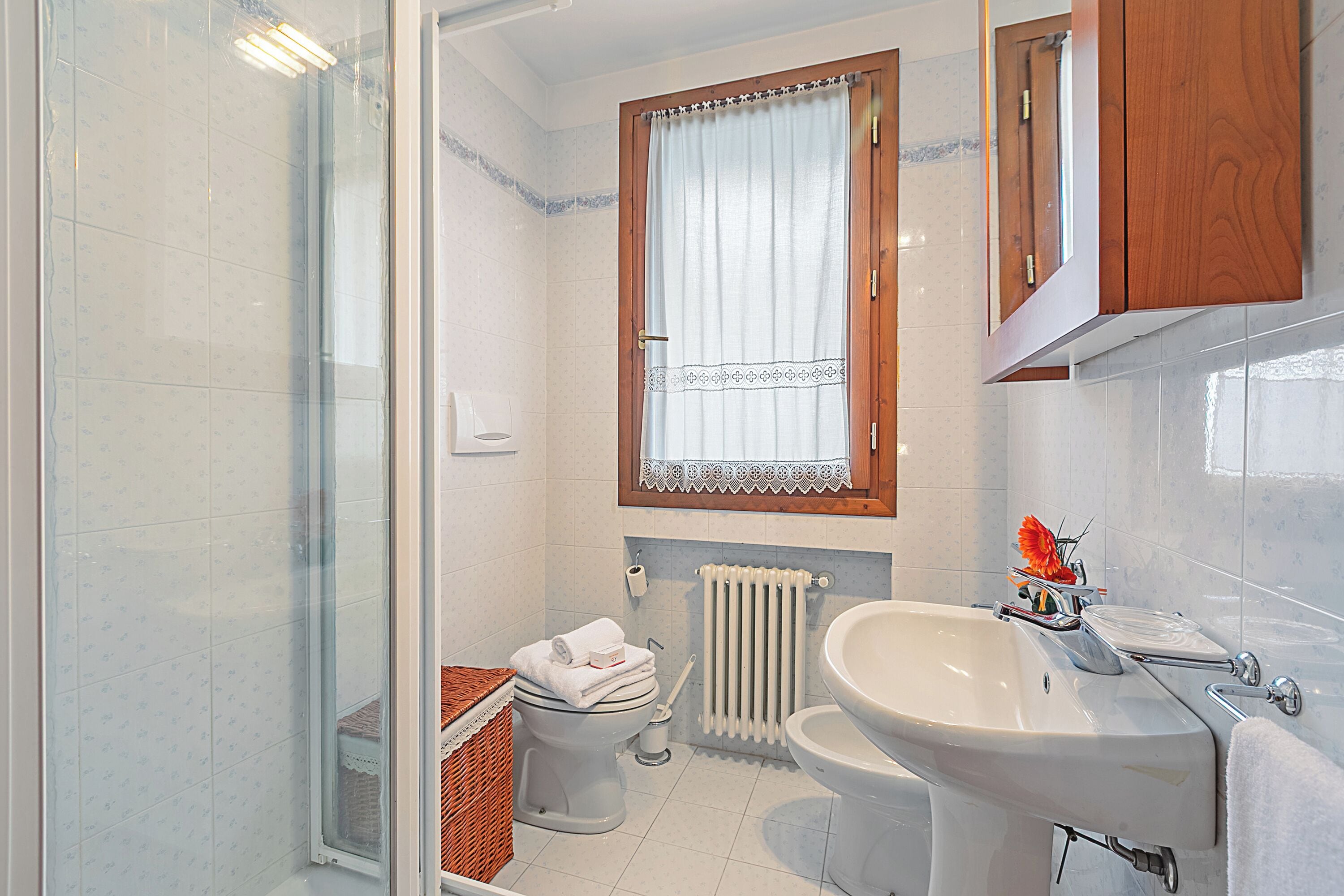 A bathroom with a shower, toilet, sink, and a window with a curtain.