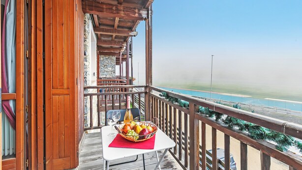 Un balcon en bois avec une table et un panier de fruits, donnant sur une plage.