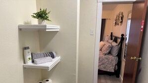 A hallway with a white shelf holding toiletries, a plant, and a rolled-up towel. - REMODELED Stellar Yellow House w/mini cine, near Plaza Mall & Downtown McAllen (McAllen)