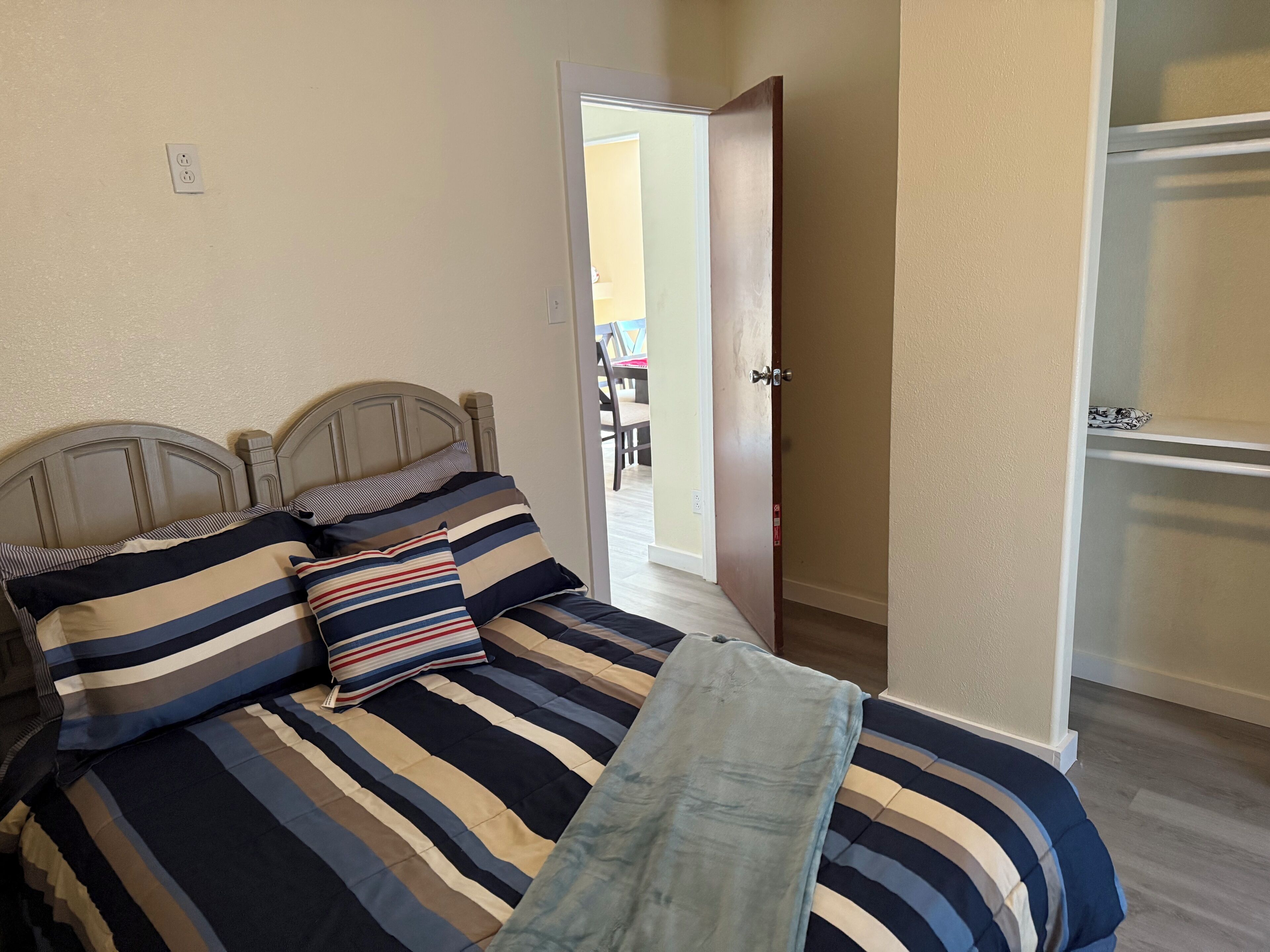 A bedroom with a bed, striped bedding, a wooden headboard, a door, and a closet.