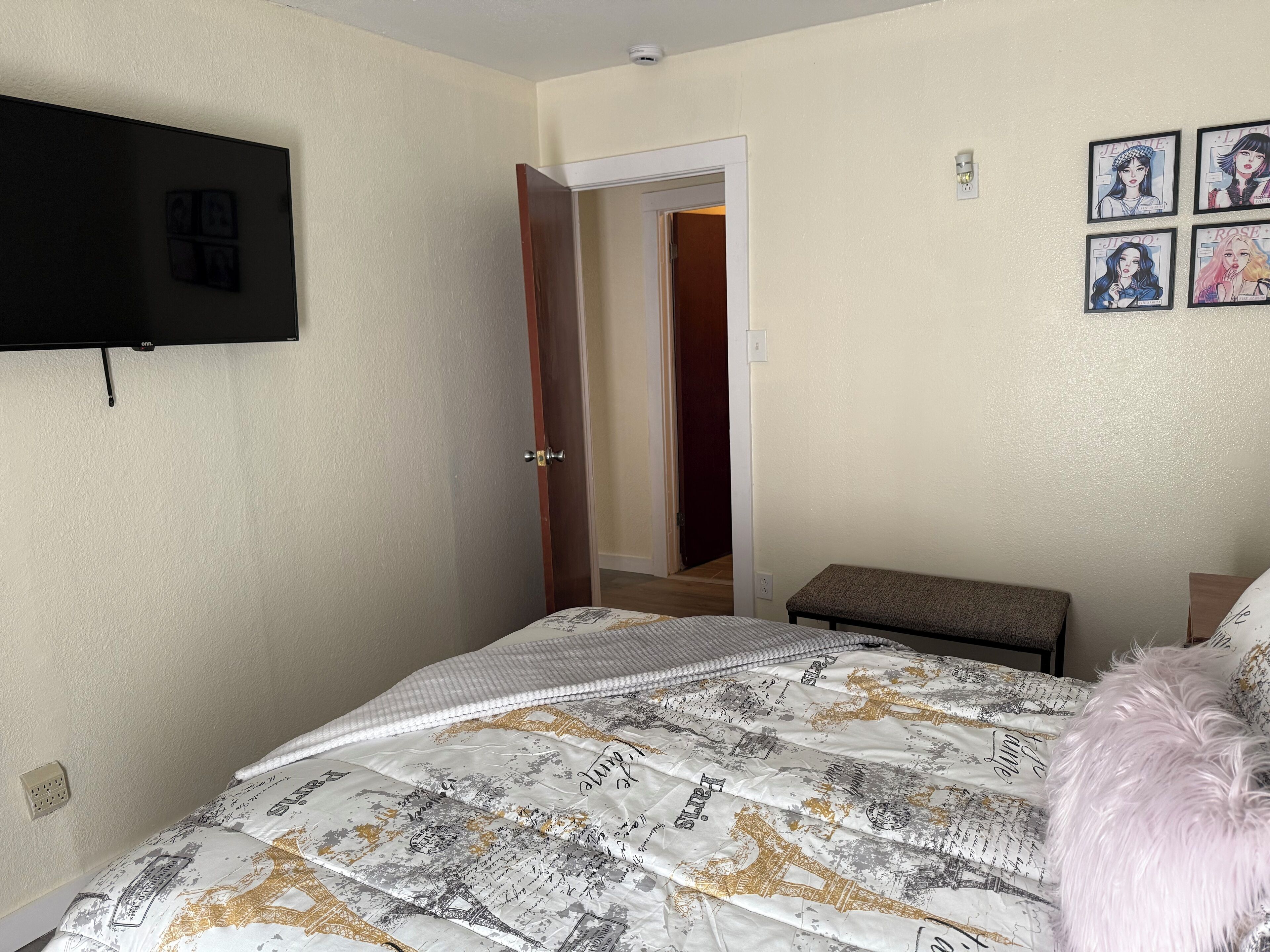 Un dormitorio con una cama, una televisión montada en la pared y una puerta que da a otra habitación.