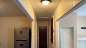 A narrow hallway with a stainless steel refrigerator on the left, a door on the right, and a ceiling light. - REMODELED Stellar Yellow House w/mini cine, near Plaza Mall & Downtown McAllen (McAllen)