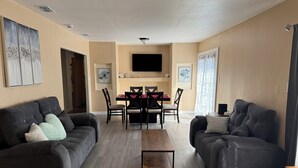 A living room with two dark sofas, a wooden coffee table, a dining table with chairs, a flat-screen TV mounted on the wall, and artwork on the walls. - REMODELED Stellar Yellow House w/mini cine, near Plaza Mall & Downtown McAllen (McAllen)