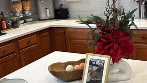Una cucina con mobili in legno, un piano di lavoro bianco, un rotolo di carta assorbente, una macchina da caffè e una decorazione festiva.