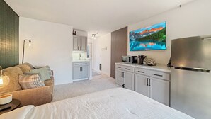 A modern hotel room with a bed, a kitchenette, a flat-screen TV, and a view of a mountain lake. - Lakeside golf Retreat • Views • ATV Trails & Pool (Hill City)