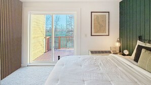 A bedroom with a large bed, a sliding glass door leading to a deck, a framed map on the wall, and a nightstand with a lamp and clock. - Lakeside golf Retreat • Views • ATV Trails & Pool (Hill City)