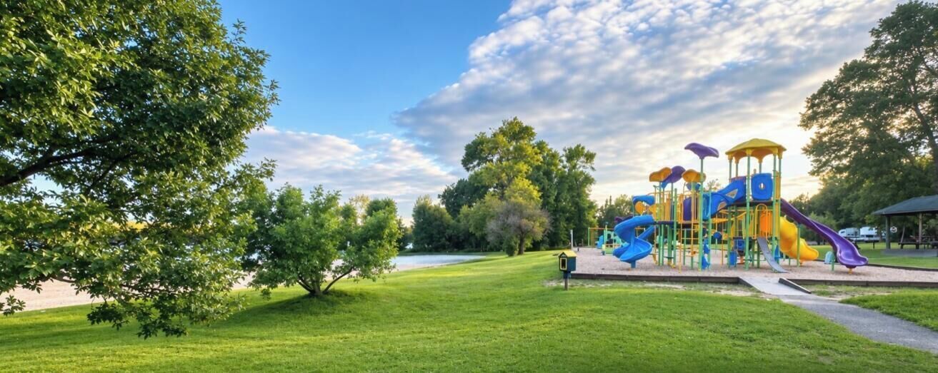 A playground with slides and climbing structures, surrounded by grass and trees.