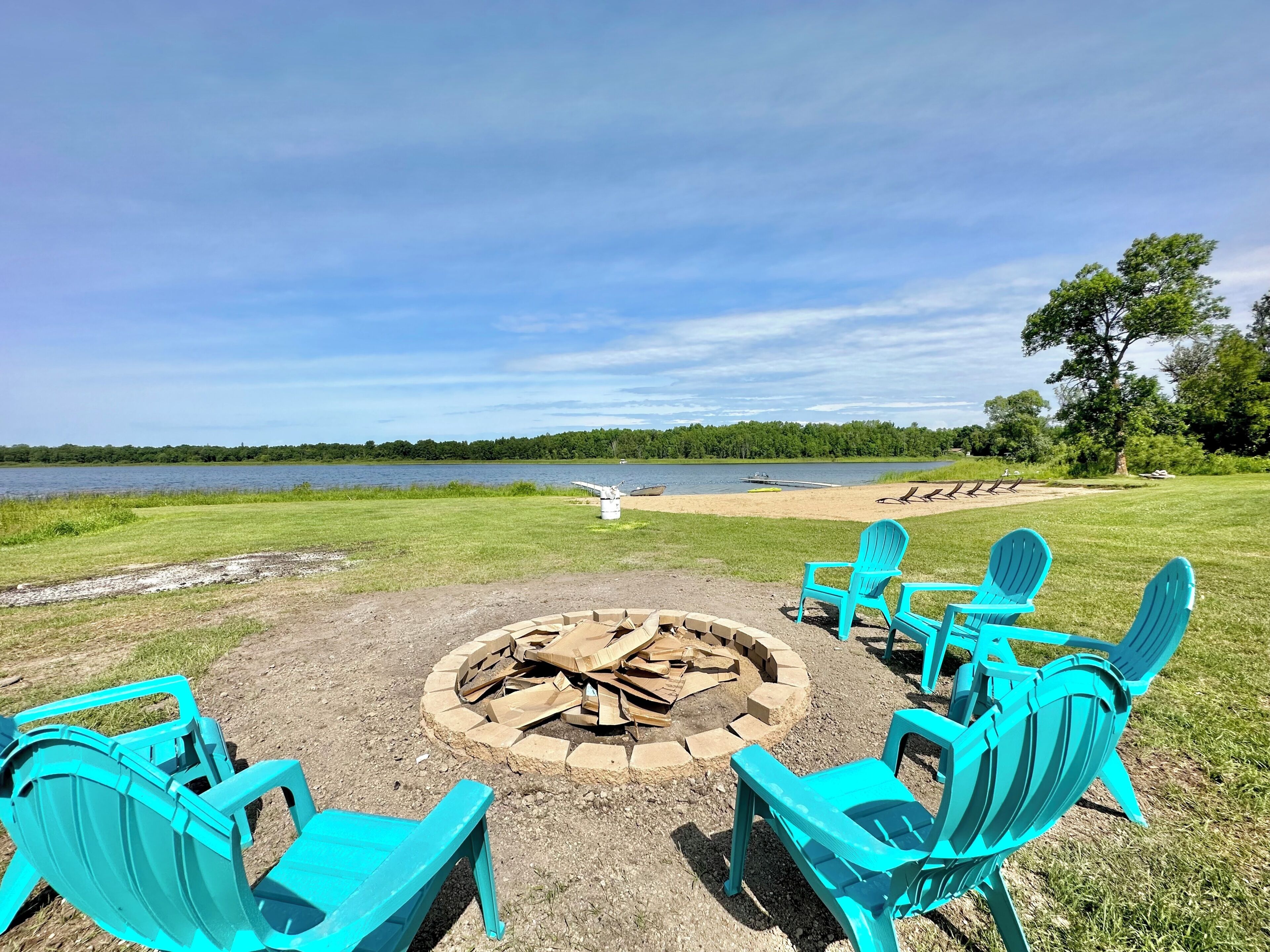 Un foyer avec des chaises disposées autour, un lac et un arbre en arrière-plan.