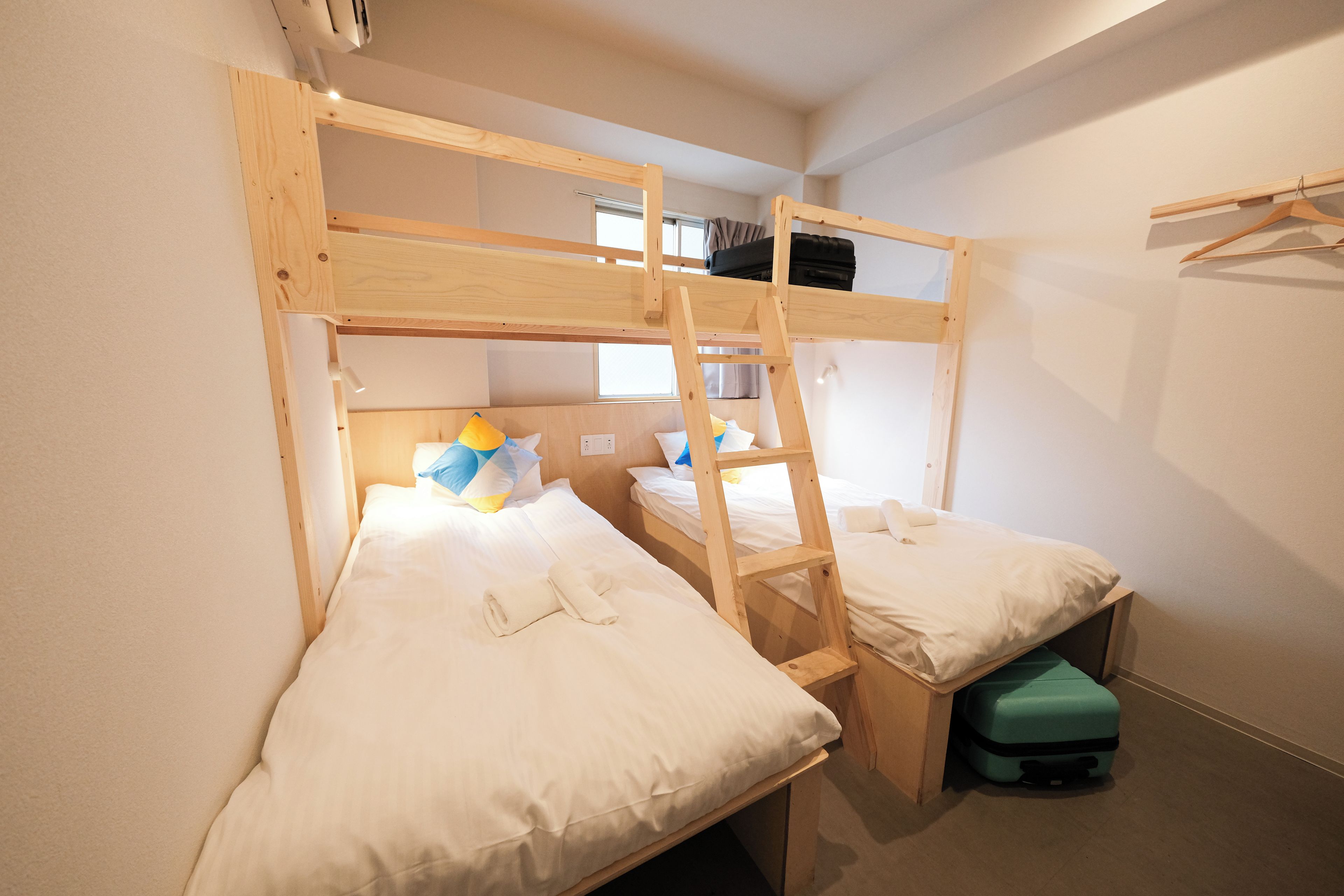 A bunk bed room with a ladder, a small table, and a suitcase.