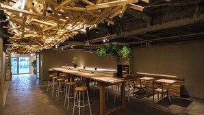 A modern interior with exposed wooden beams, a long bar area with stools, and a potted plant. - 2Z - DOYANEN HOTELS (Osaka)